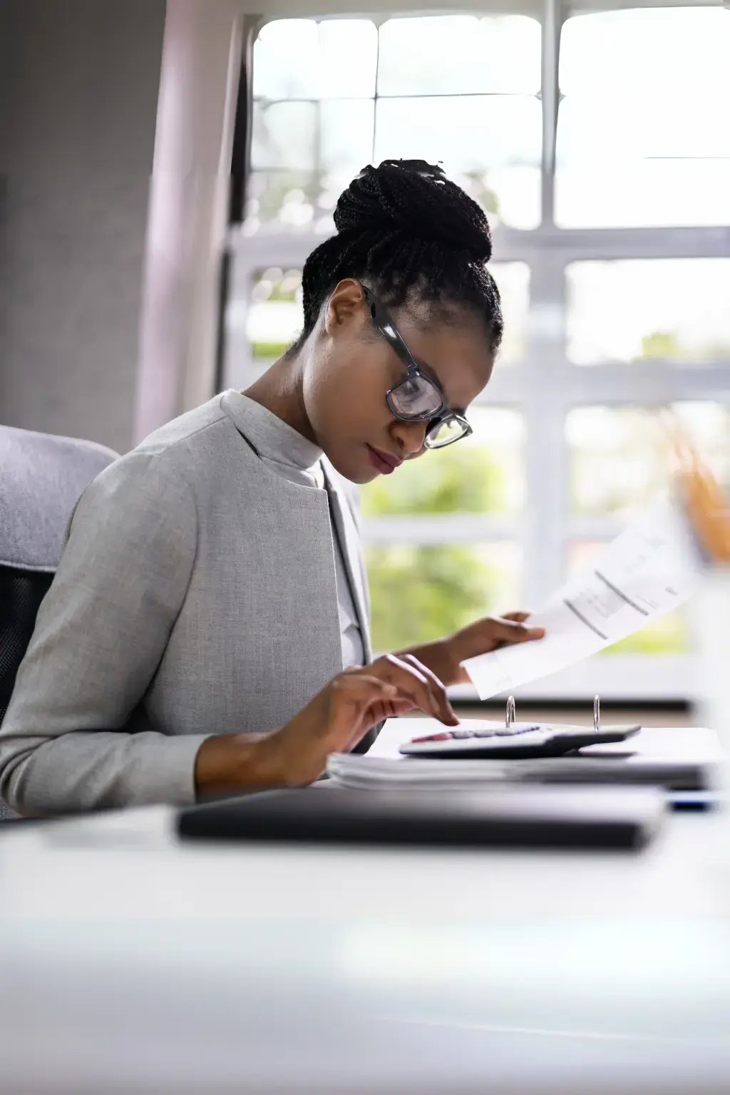 Accountant reviewing financial documents and using a calculator at her desk in a bright office.