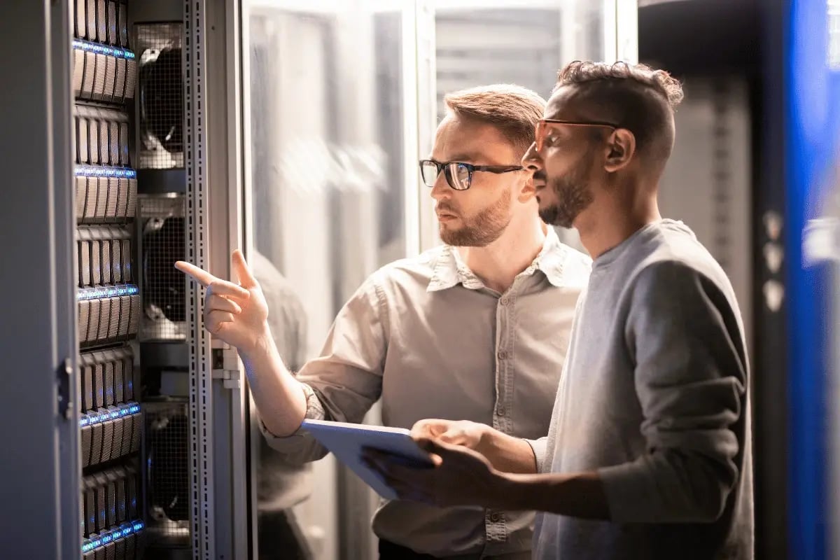 Two IT technicians inspecting server racks and performing maintenance in a data center